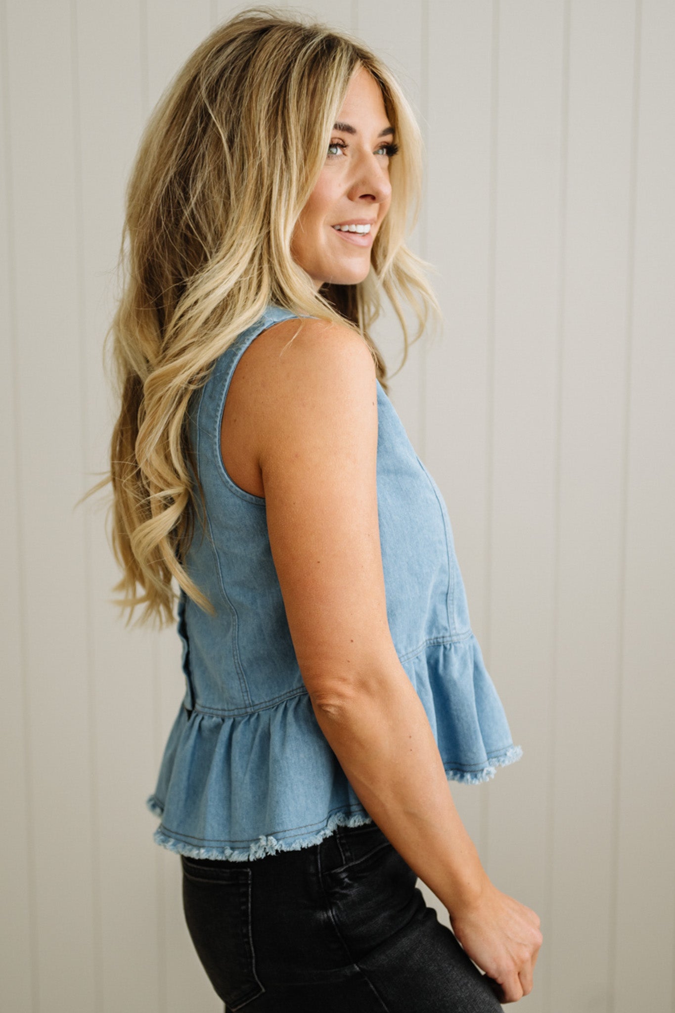 Woman wearing a denim sleeveless top with ruffled details against a neutral background