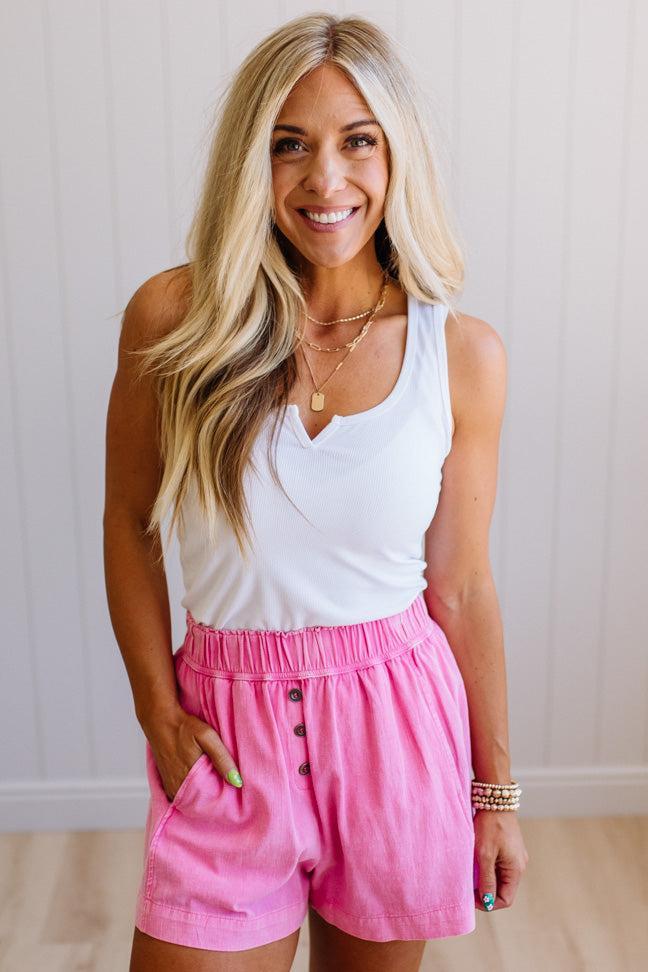 Woman wearing a white tank top and pink shorts with a neutral background