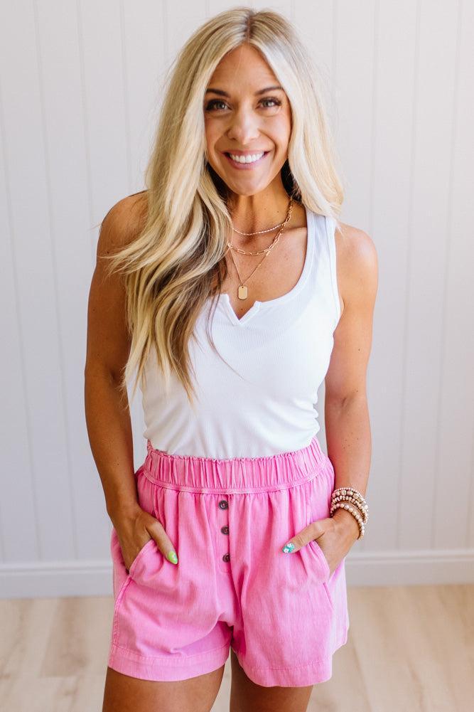 Woman wearing a white tank top and pink shorts with a neutral background