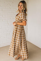 Woman wearing a plaid dress standing against a white brick wall.