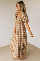 Woman wearing a plaid dress standing against a white brick wall.