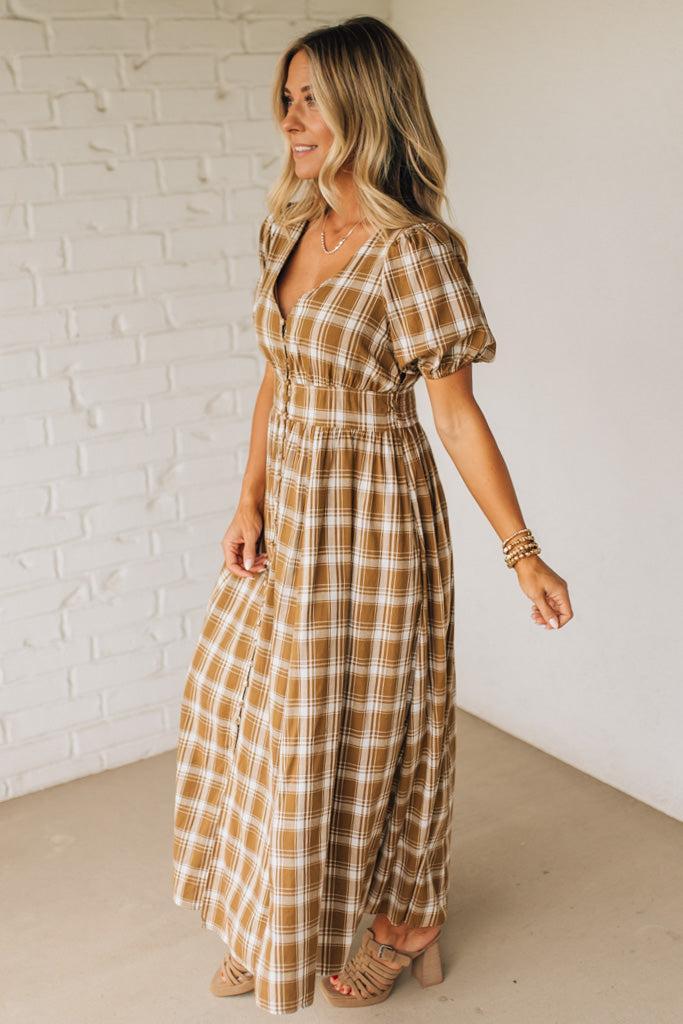 Woman wearing a plaid dress standing against a white brick wall.
