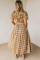Woman wearing a plaid dress standing against a white brick wall.