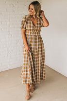 Woman wearing a plaid dress against a white brick wall.