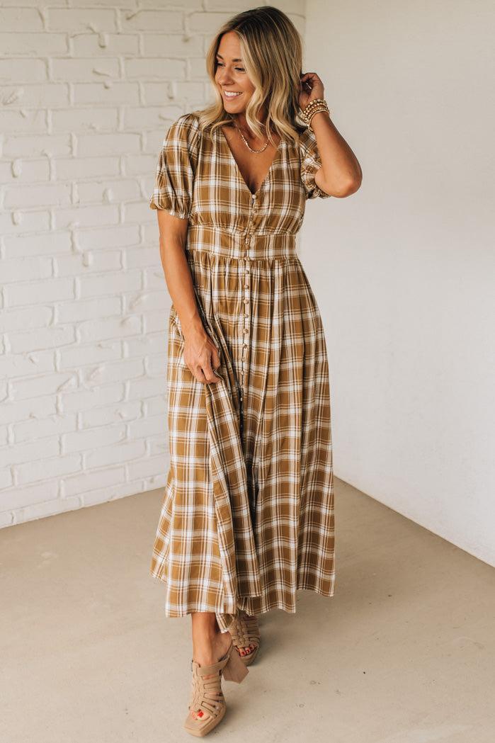 Woman wearing a plaid dress against a white brick wall.