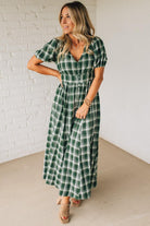 Woman wearing a green plaid dress against a white brick wall.
