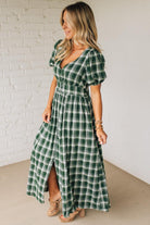 Woman wearing a green plaid dress against a white brick wall.