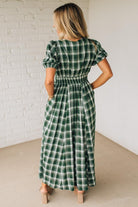 Woman wearing a green plaid dress against a white brick wall.