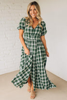 Woman wearing a green plaid dress against a white brick wall.