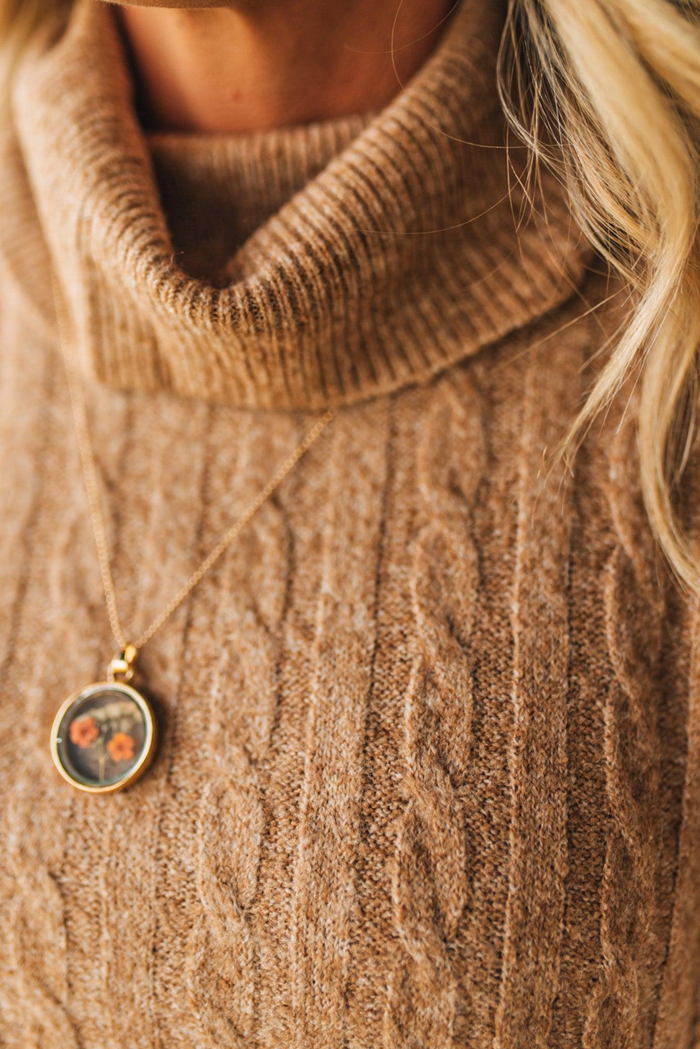 Close-up of a person wearing a brown sweater with a necklace featuring a round pendant.