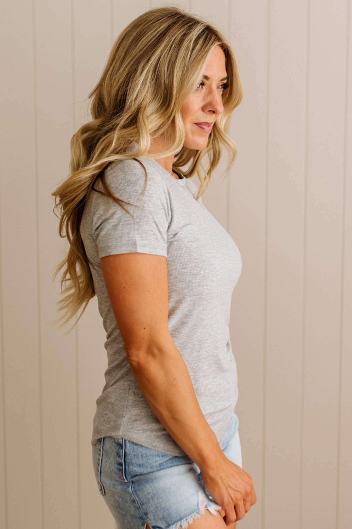Woman wearing a gray t-shirt and denim shorts against a beige wall.