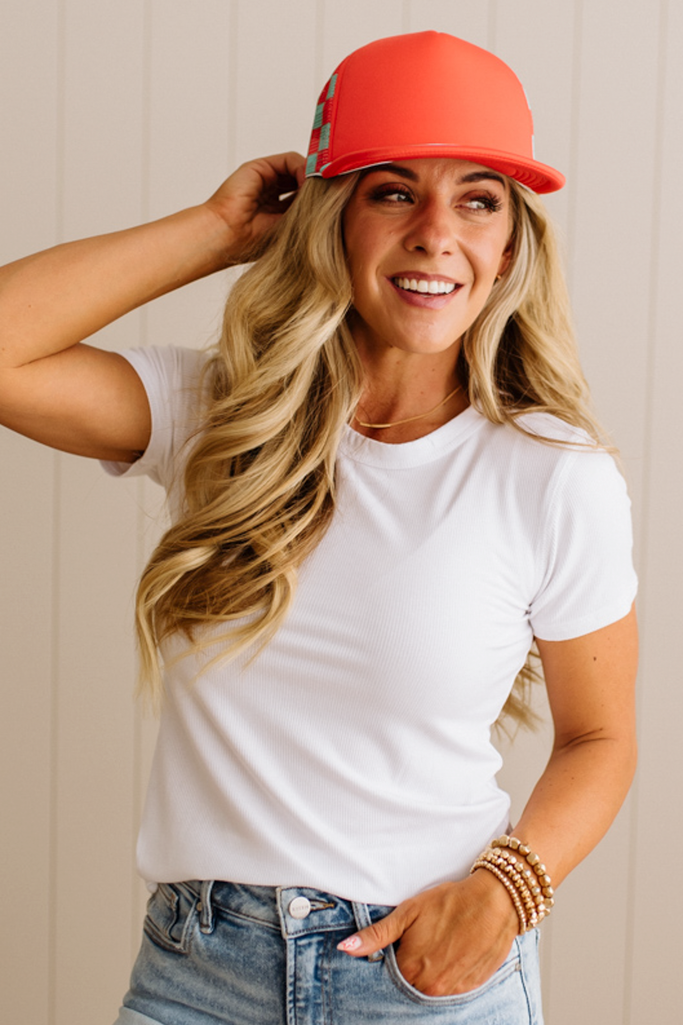 Woman wearing a white t-shirt, red cap, and blue jeans against a beige background