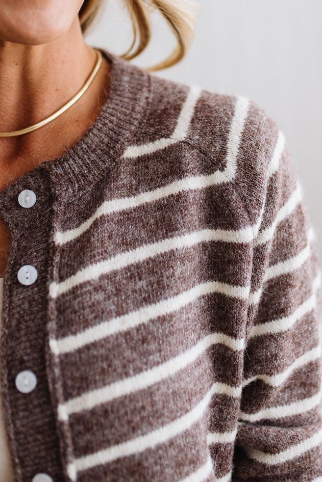 BLONDE WOMAN IN A BRIGHTLY LIT STUDIO WEARING A CREAM TANK AND DARK JEANS SHOWING A OUTSEAMED, LONG SLEEVE, FUZZY, CREW NECK STRIPED BUTTON DOWN SWEATER CARDIGAN IN CHOCOLATE MOCHA.