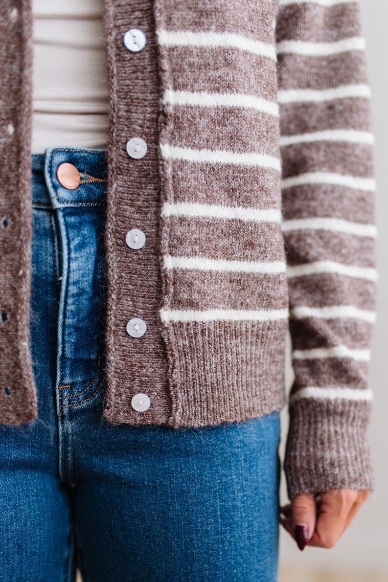 BLONDE WOMAN IN A BRIGHTLY LIT STUDIO WEARING A CREAM TANK AND DARK JEANS SHOWING A OUTSEAMED, LONG SLEEVE, FUZZY, CREW NECK STRIPED BUTTON DOWN SWEATER CARDIGAN IN CHOCOLATE MOCHA.
