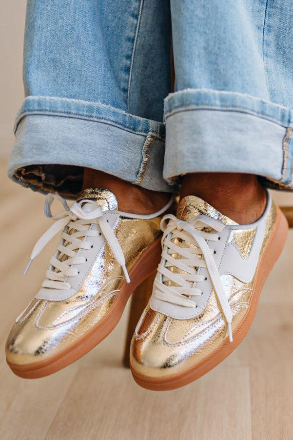Woman wearing metallic gold and white slip-on sneakers featuring a bold swoosh pattern on the side, giving them a dynamic, sporty look. The durable gum sole provides excellent traction and a retro touch.