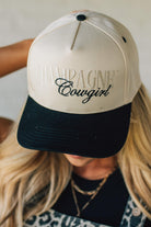Blonde woman wearing a cream and black trucker hat with "Champagne Cowgirl" embroidered at the front.