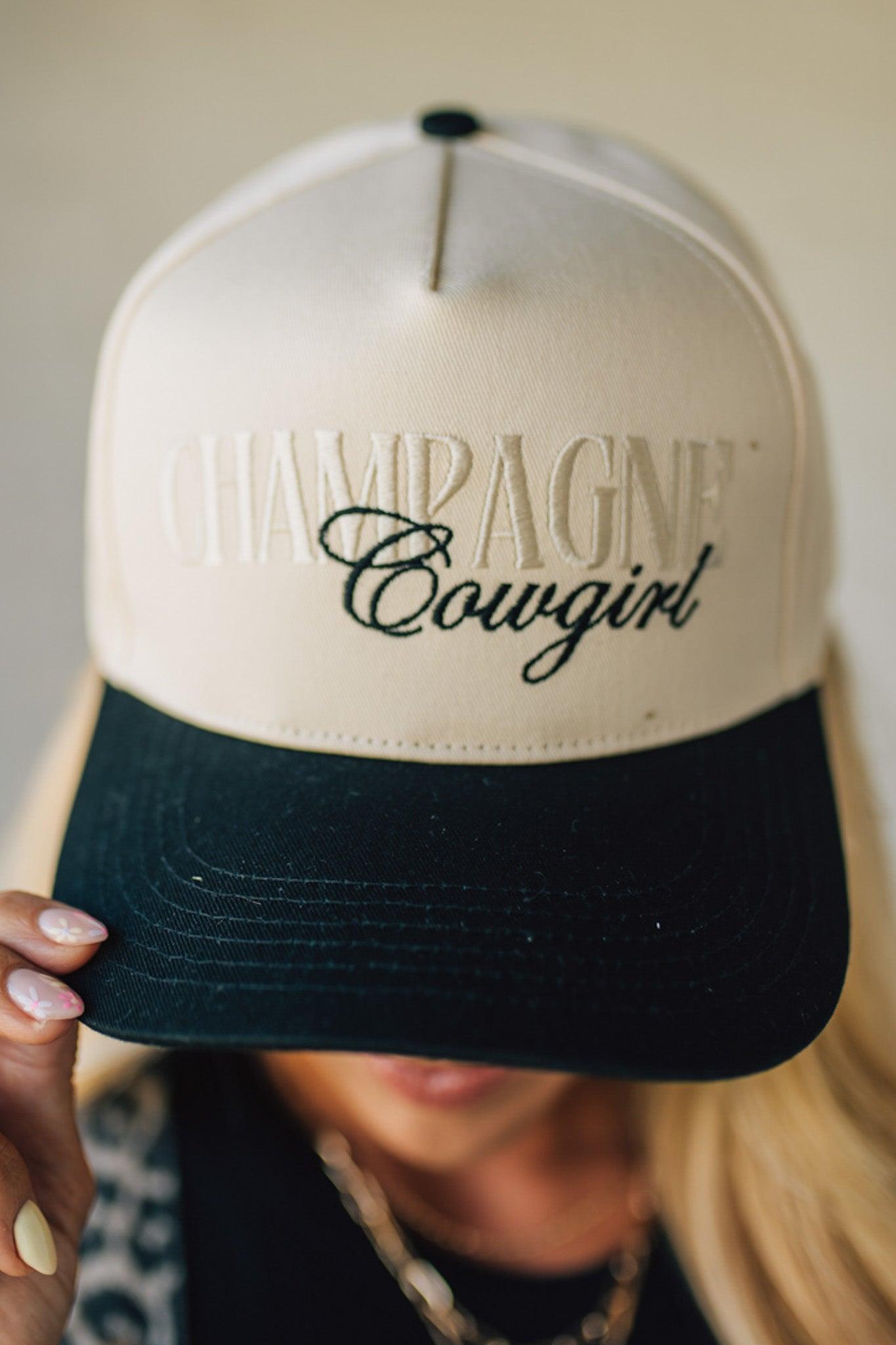 Blonde woman wearing a cream and black trucker hat with "Champagne Cowgirl" embroidered at the front.
