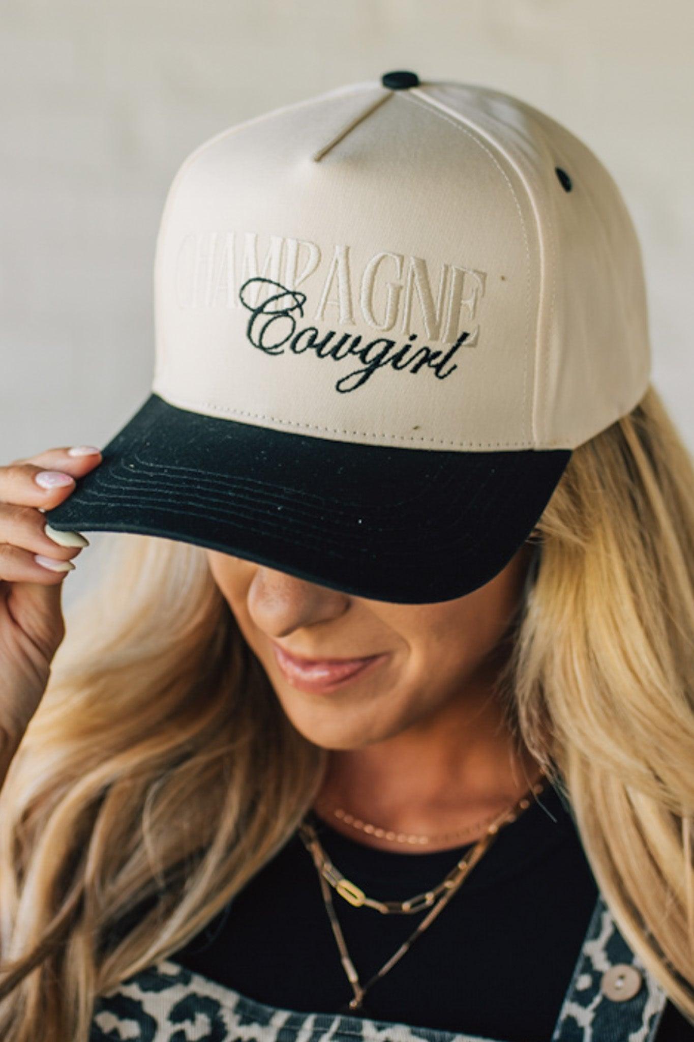 Blonde woman wearing a cream and black trucker hat with "Champagne Cowgirl" embroidered at the front.
