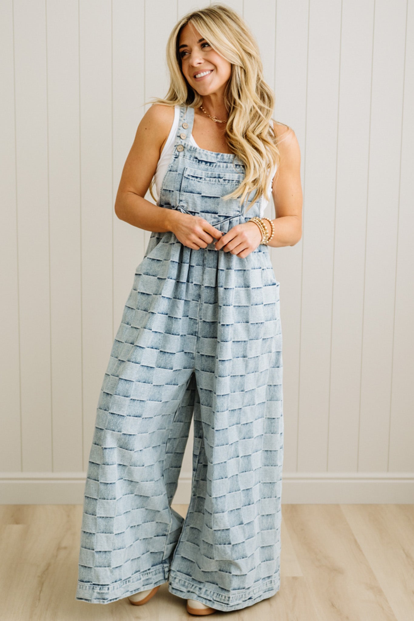 Woman wearing a blue patterned jumpsuit standing against a white paneled wall.
