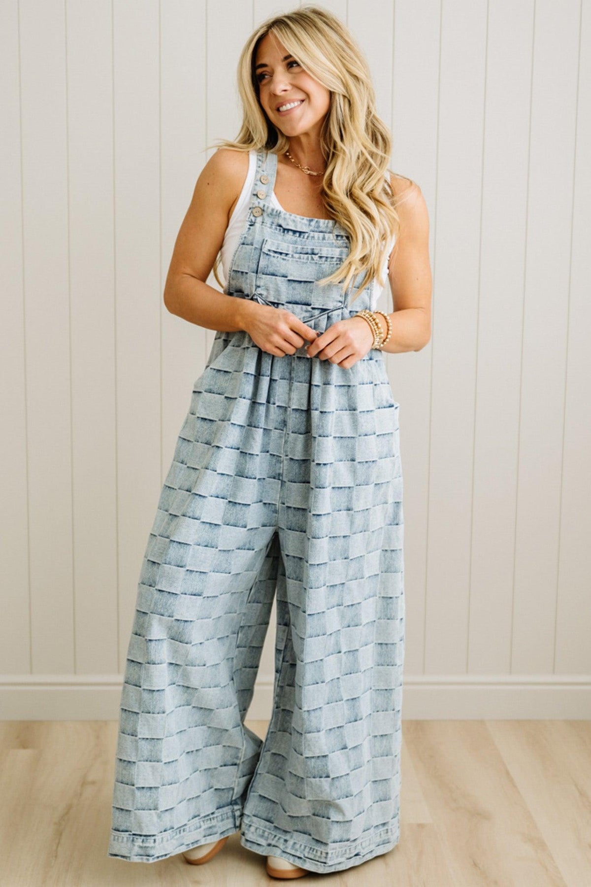 Woman wearing a blue patterned jumpsuit standing against a white paneled wall.
