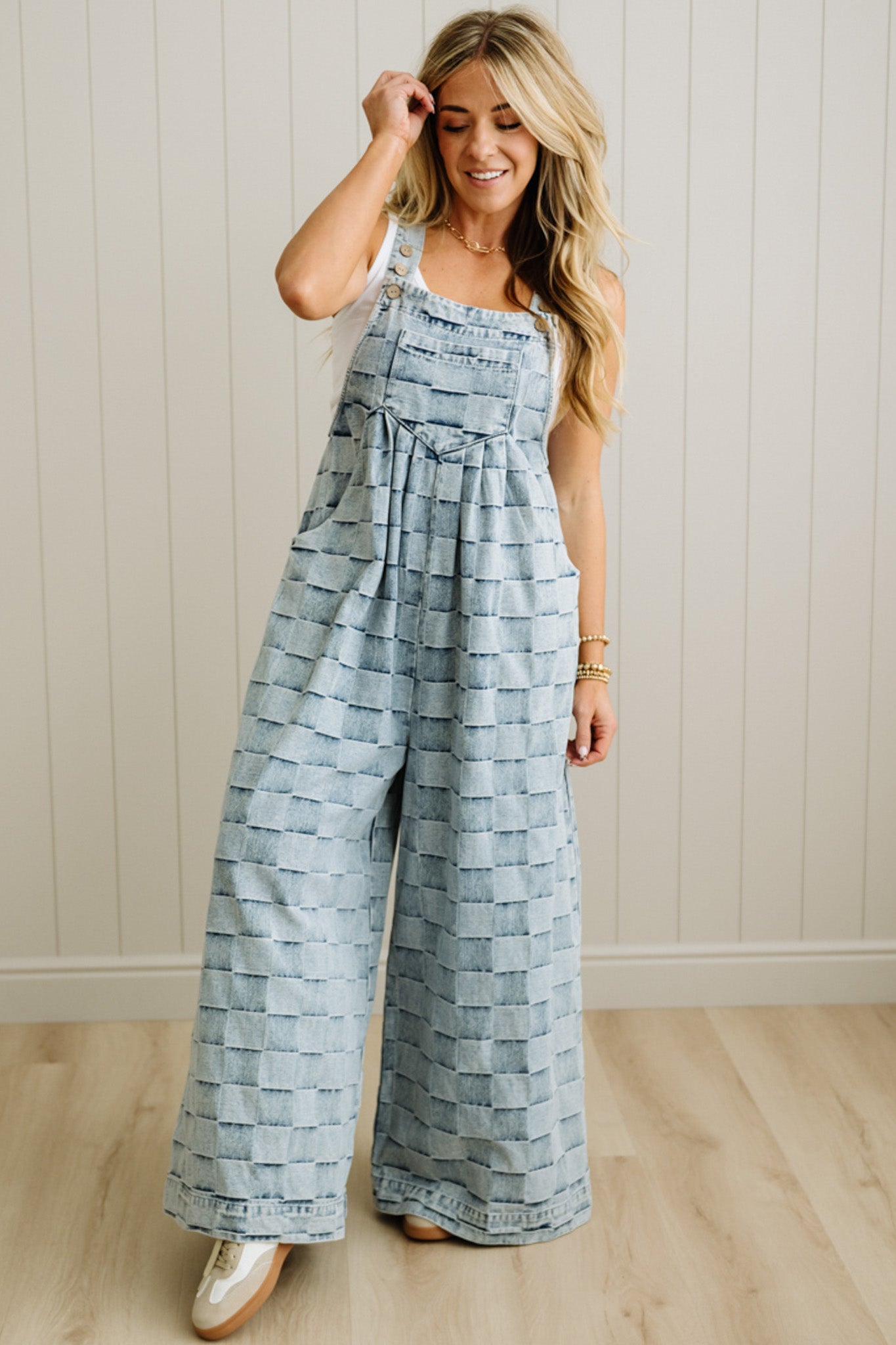 Woman wearing a patterned jumpsuit standing against a light wooden paneled wall.