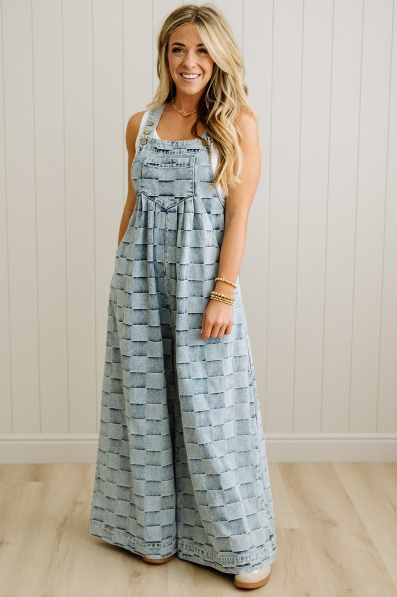 Woman wearing a blue patterned jumpsuit standing against a white paneled wall.