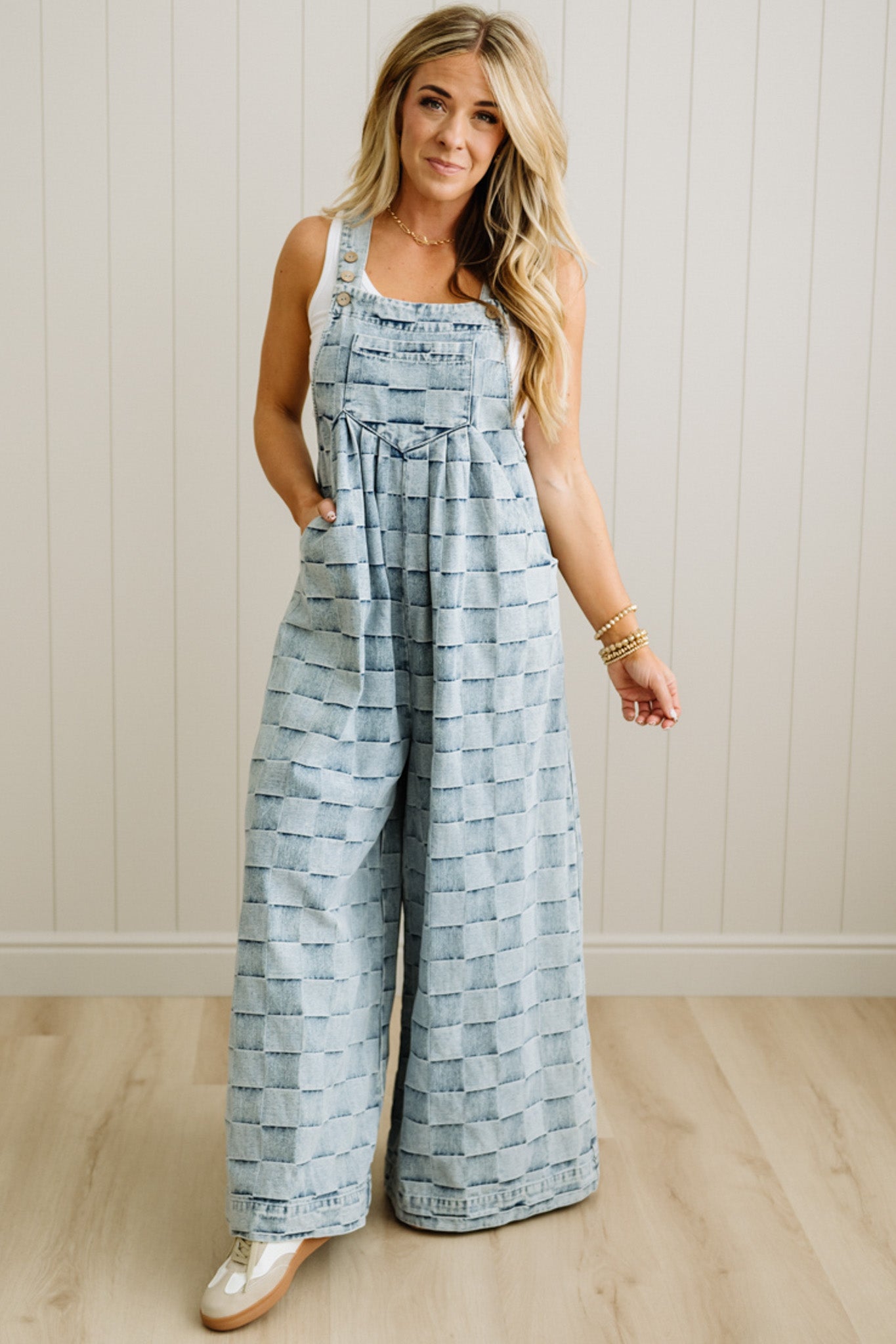 Woman wearing a patterned jumpsuit standing against a white paneled wall.