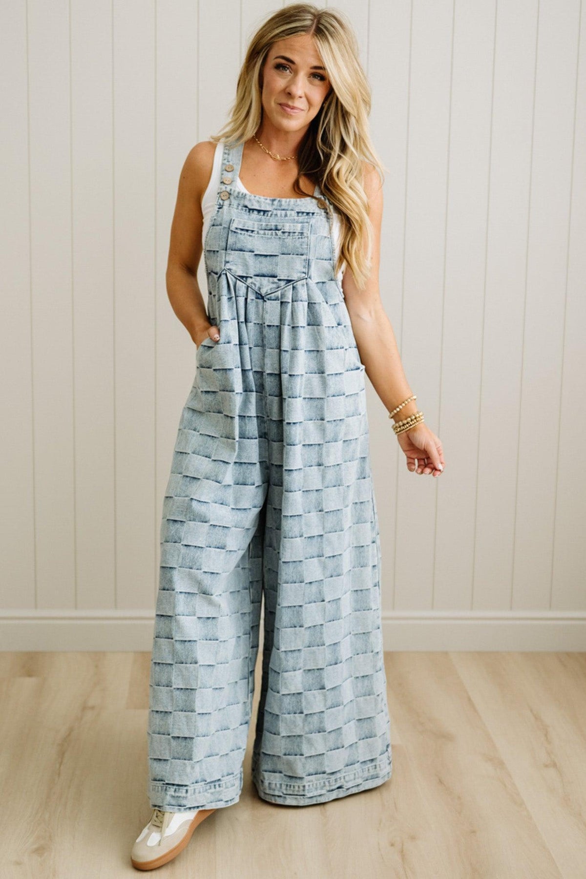 Woman wearing a patterned jumpsuit standing against a white paneled wall.