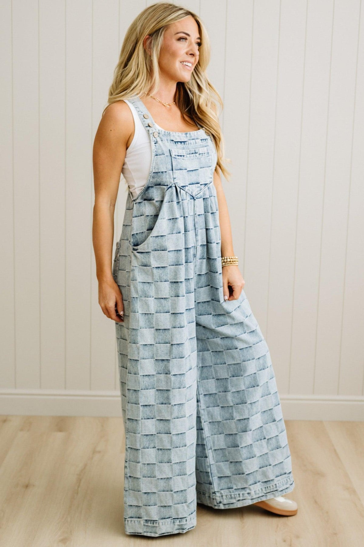 Woman wearing a blue checkered jumpsuit standing against a white wall.