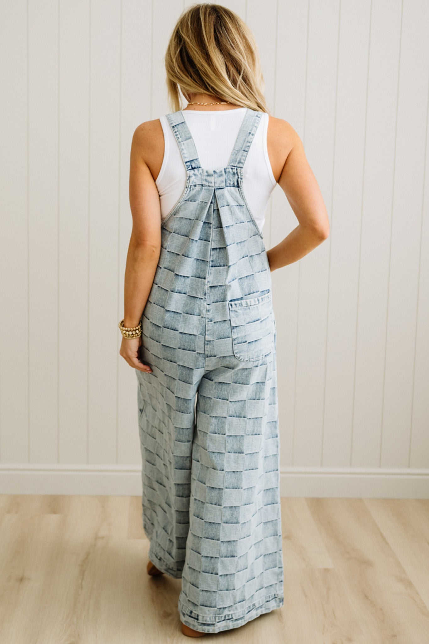 Woman wearing a patterned overalls standing against a white wall.
