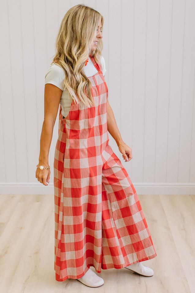 Blonde woman in a studio with light wood floors and a light backdrop, wearing a tee-shirt and latte/orage wide leg jumpsuit.