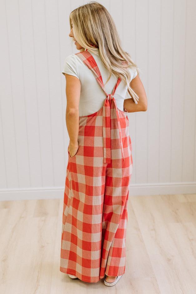 Blonde woman in a studio with light wood floors and a light backdrop, wearing a tee-shirt and latte/orage wide leg jumpsuit.