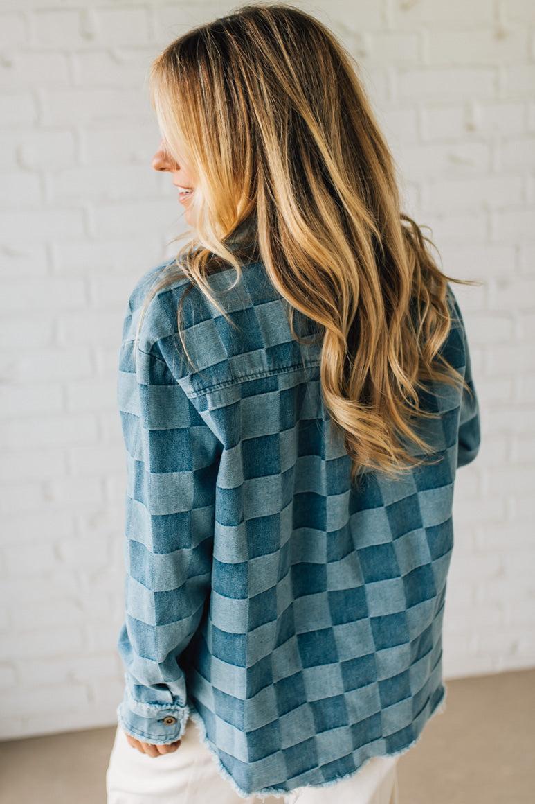 Woman wearing a blue checkered shirt against a white brick wall.