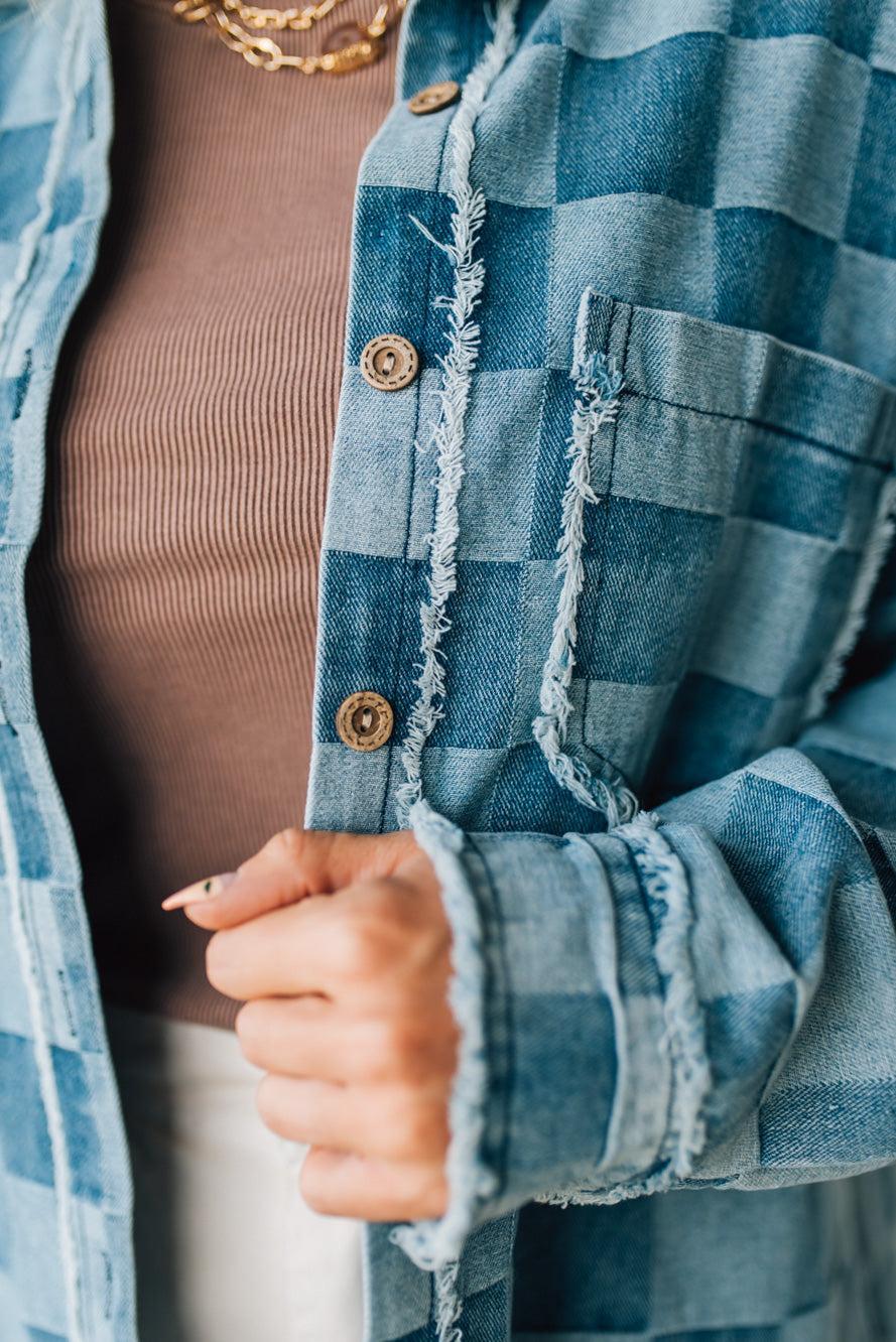 Close-up of a person wearing a blue plaid shirt with a brown sweater underneath.