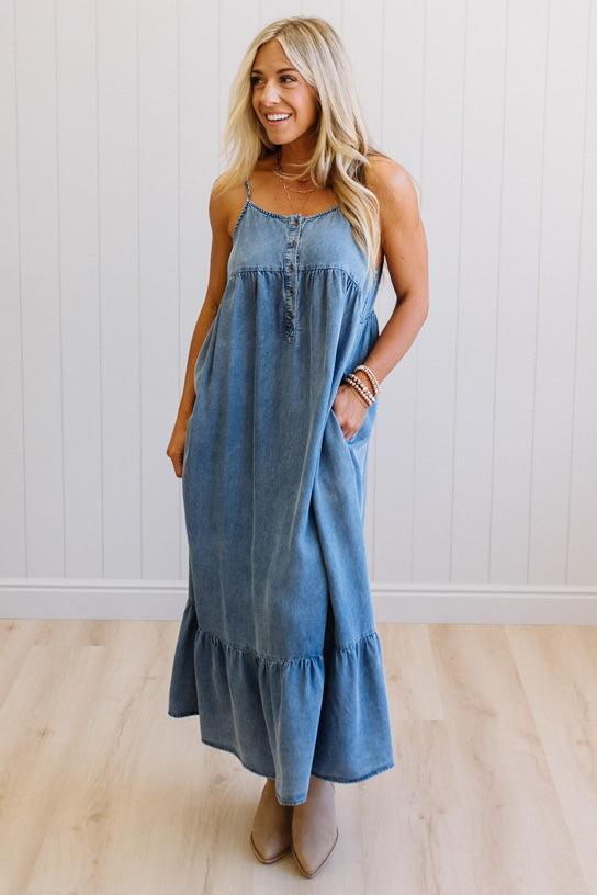 Woman wearing a blue denim dress standing against a white wall.