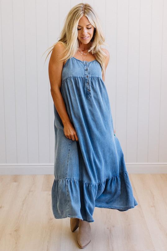 Woman wearing a blue denim dress standing against a white wall.