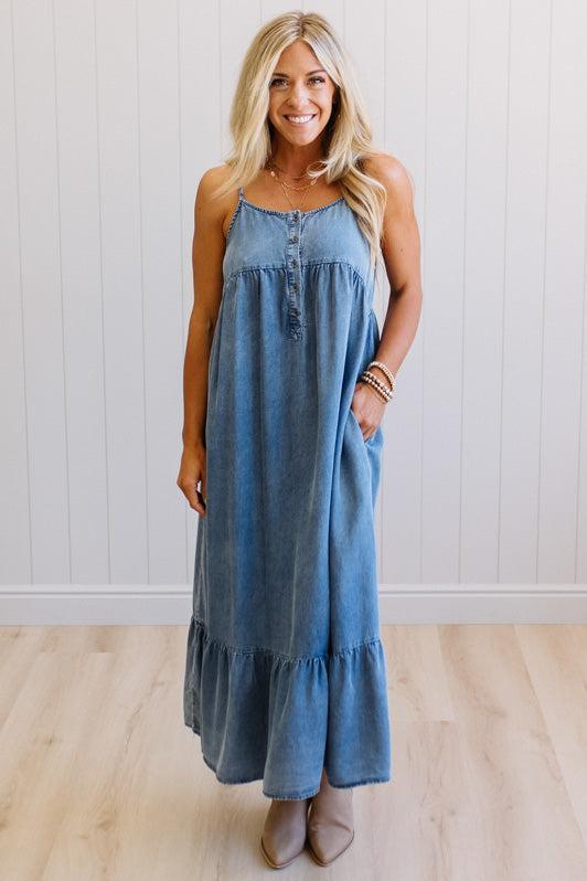Woman wearing a blue denim dress standing against a white wall.