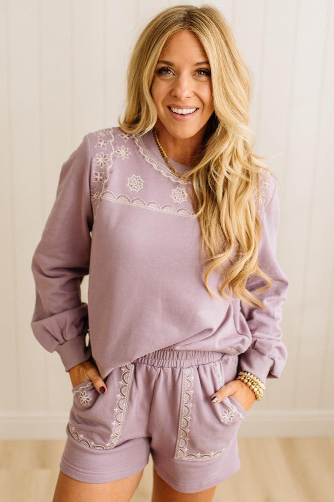 Woman wearing a matching lavender outfit with embroidered details on a plain background