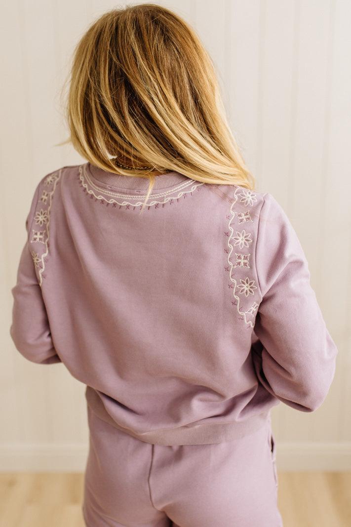 Person wearing a mauve outfit with intricate white embroidery on a plain background
