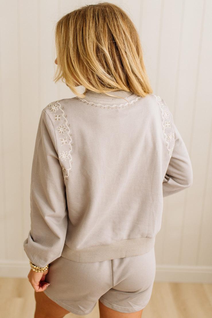 Person wearing a light gray outfit with lace details on a plain background