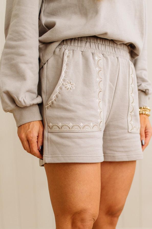 Light gray shorts with white embroidery on a neutral background