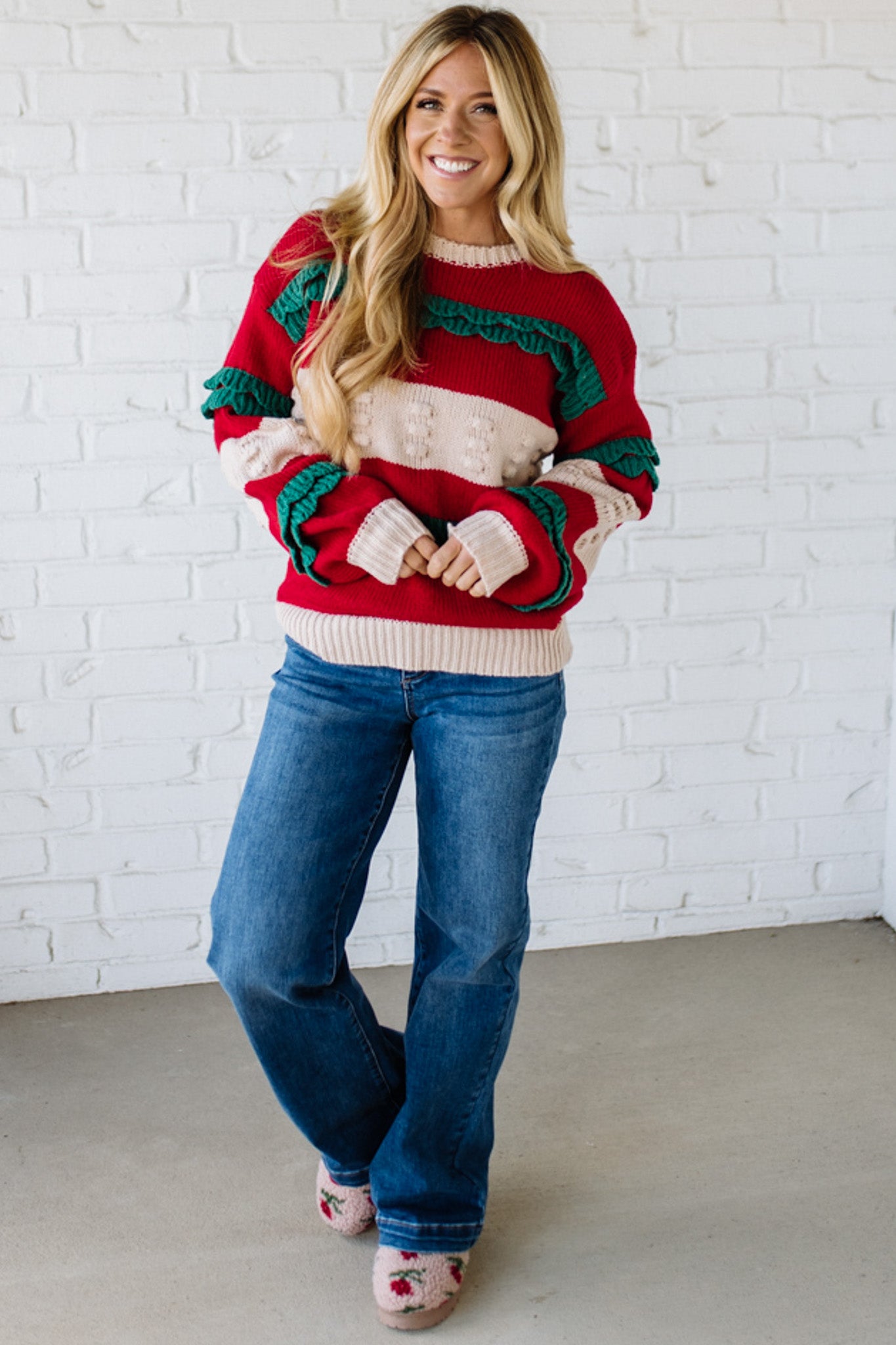 BLONDE WOMAN WEARING A CHRISTMAS THEME RUFFLED DETAILS SWEATER TOP IN RED, CREAM, AND HUNTER GREEN.