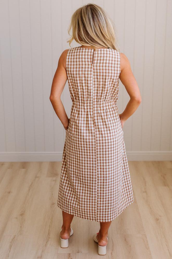 Woman wearing a checkered dress standing against a plain wall.