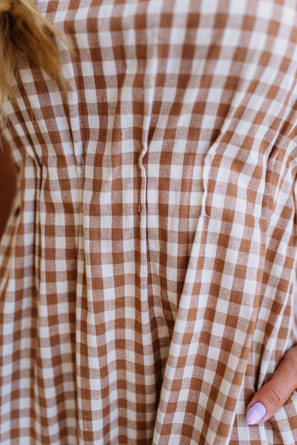 Woman wearing a checkered dress standing against a plain wall.