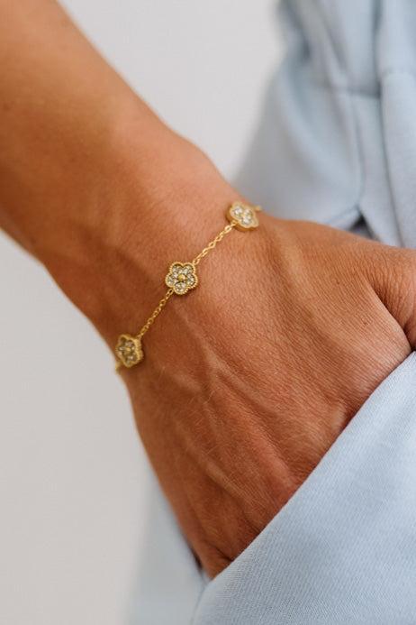 Gold bracelet with floral designs on a wrist against a light background