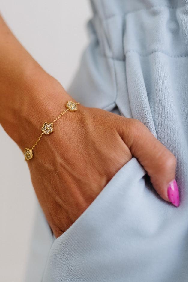 Gold bracelet on a wrist with a light blue garment in the background