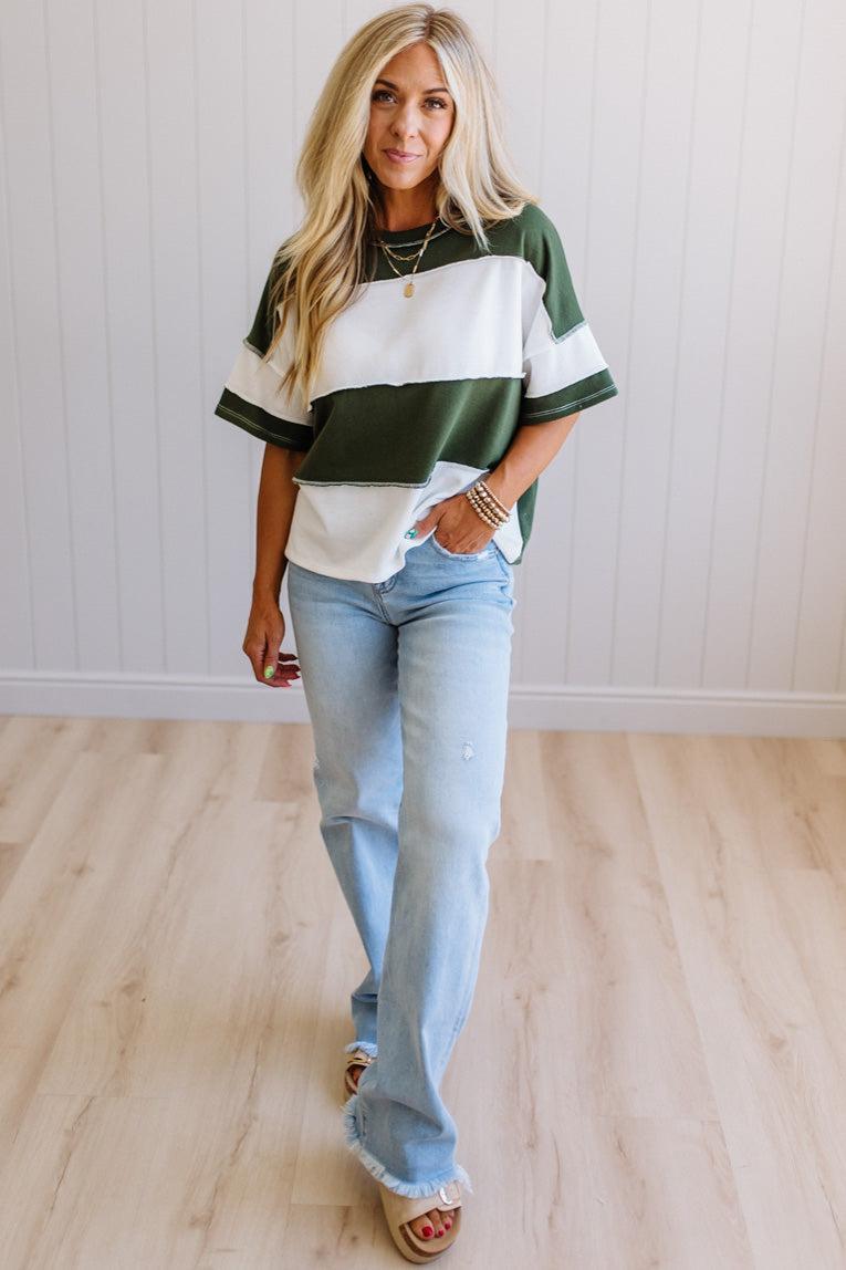 Woman wearing a green and white striped shirt with blue jeans indoors.