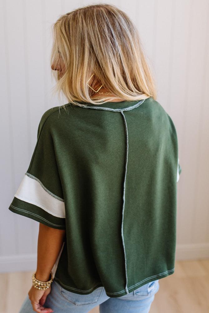 Person wearing a green poncho with white trim, standing against a plain background