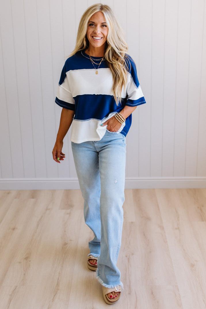 Woman wearing a blue and white striped shirt and light blue jeans standing against a white wall.