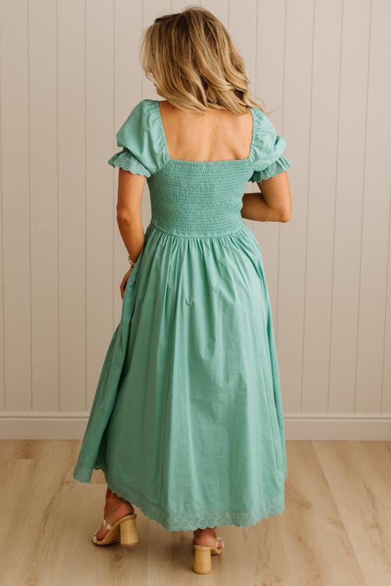 Woman wearing a green dress with ruffled sleeves against a beige wall.